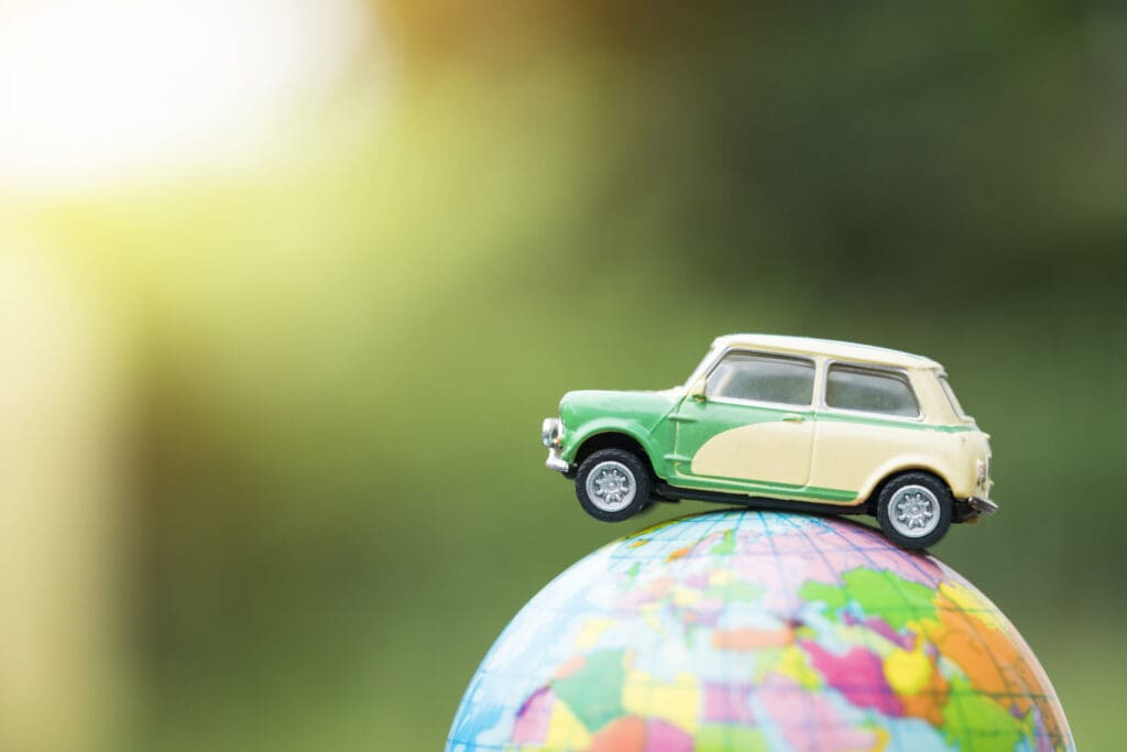Travel and transport concept. Toy car on world map balloon with green nature background.