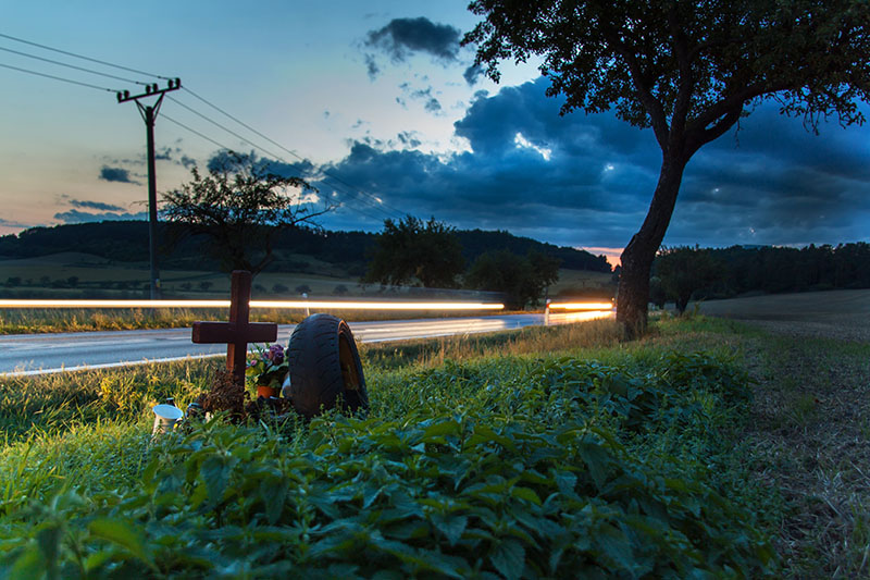 Lights of moving cars on a rural road. Evening in the place of a fatal accident. Place a car accident at the crossroads