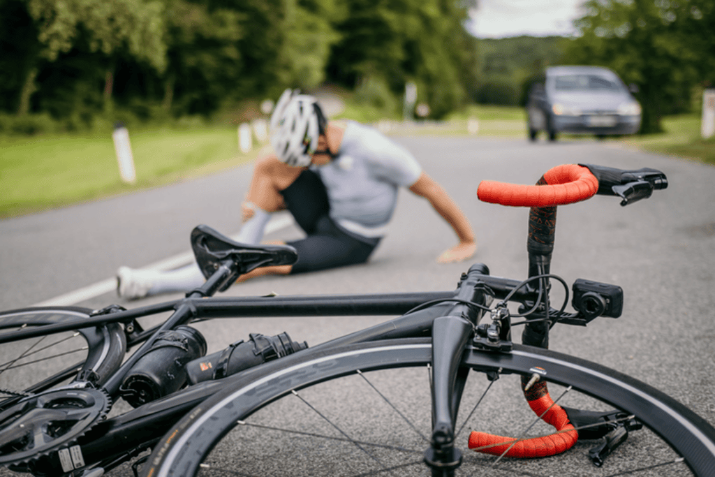 Bike on ground in foreground. Bicyclist sitting, holding shin in background
